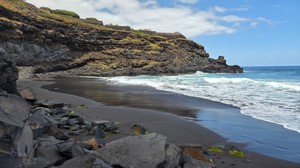 Black sand beach at Playa El Ancón with rugged cliffs and ocean waves.