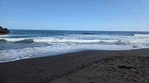 Footprints in the black sand at Playa El Ancón with waves approaching.