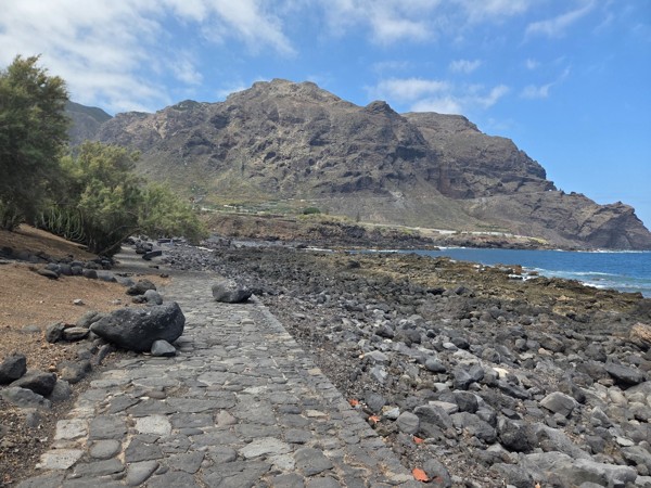 Section of the seaside promenade bordered by tamarisk trees and volcanic rocks at Playa de Las Arenas.