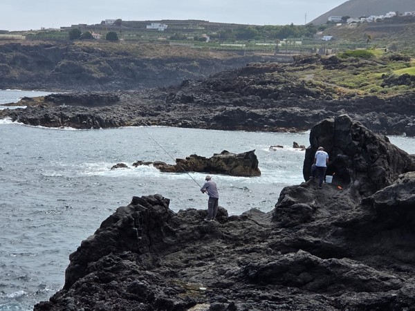 Local anglers casting lines from jagged lava cliffs opposite the beach.