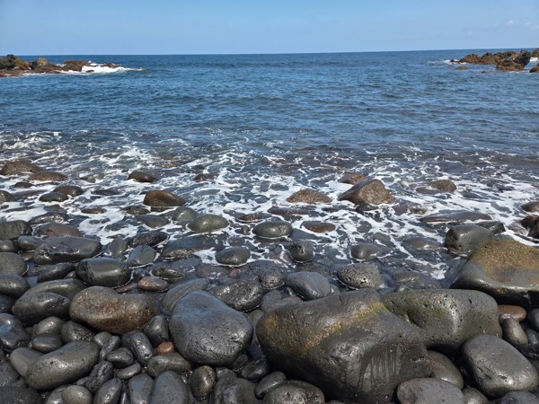 Smooth basalt pebbles glistening where the surf meets the shore.
