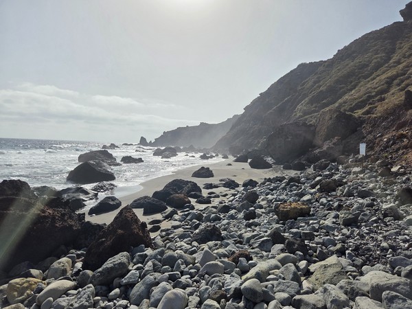 Wide view of Playa de las Breñas with dark sand, volcanic rocks, and steep cliffs under soft sunlight.