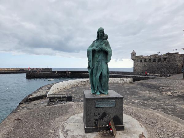 Bronze statue of the Virgin Mary holding a child, facing the sea near Playa del Muelle.