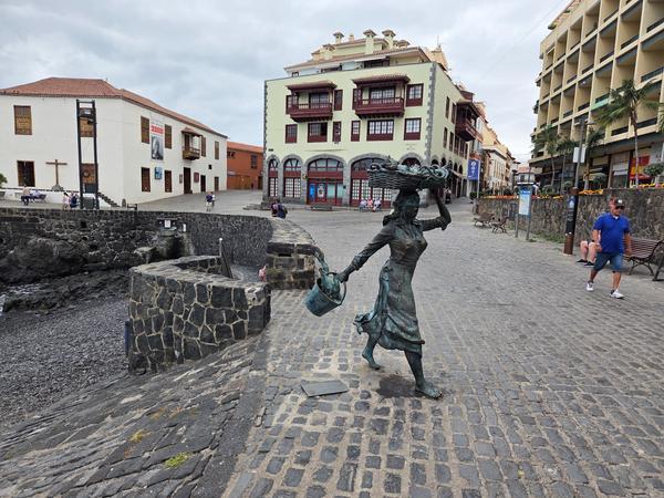 Bronze statue of a fisherwoman balancing a basket on her head in front of Playa del Muelle.