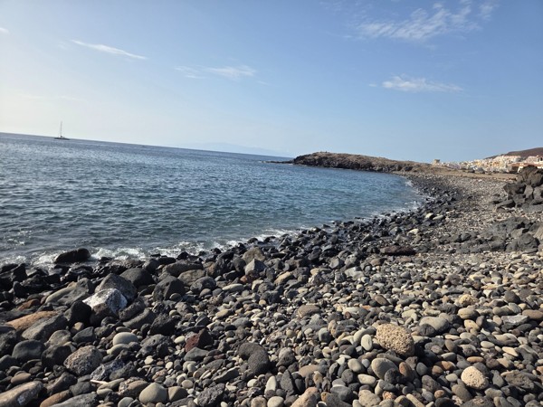 Wide pebble shore of Playa El Callao with rounded volcanic stones leading into the Atlantic Ocean and a low headland in the background.