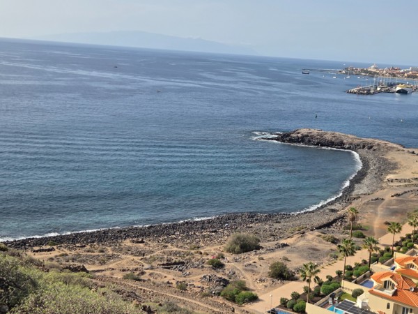Panoramic aerial view of Playa El Callao in Arona with its curved pebble beach, volcanic coastline and the harbour of Los Cristianos in the distance.