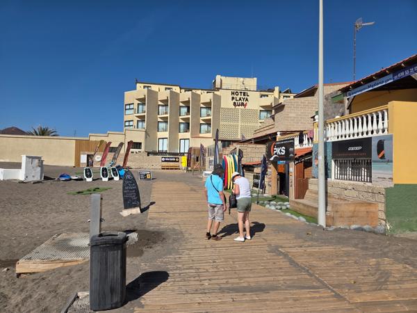 Boardwalk leading to Playa El Médano with surf shops and Hotel Playa Sur in the background.