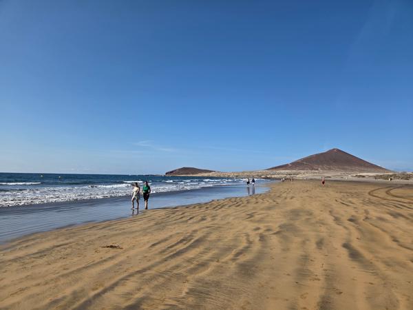 Wide sandy shore of Playa El Médano with Montaña Roja in the background.