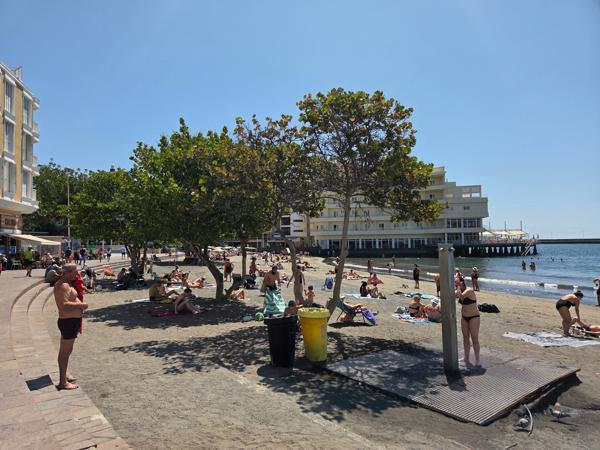 Visitors walking along the shore of Playa El Médano enjoying the sunny weather.