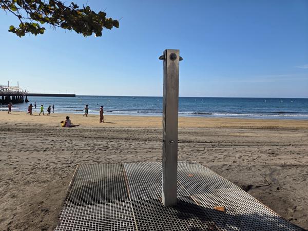 Outdoor beach shower at Playa El Médano with children and families in the distance.