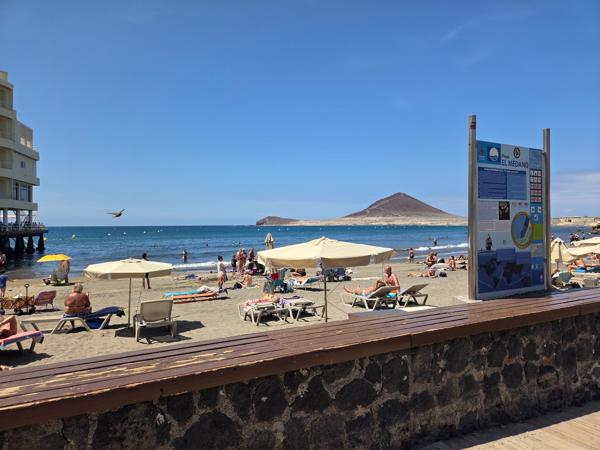 Information sign at Playa El Médano with beachgoers and umbrellas in view.
