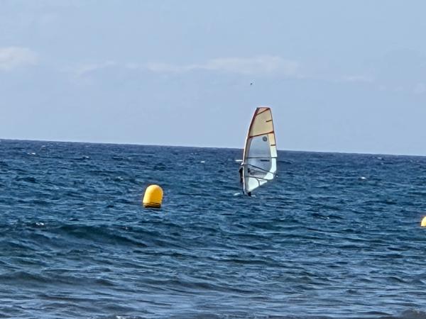 Windsurfer navigating the open sea near Playa El Médano with yellow buoys nearby.