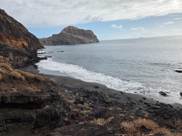 Wide view of Playa Itamar Diez from the cliffs, with a long strip of black sand and a rocky headland jutting into the Atlantic Ocean.