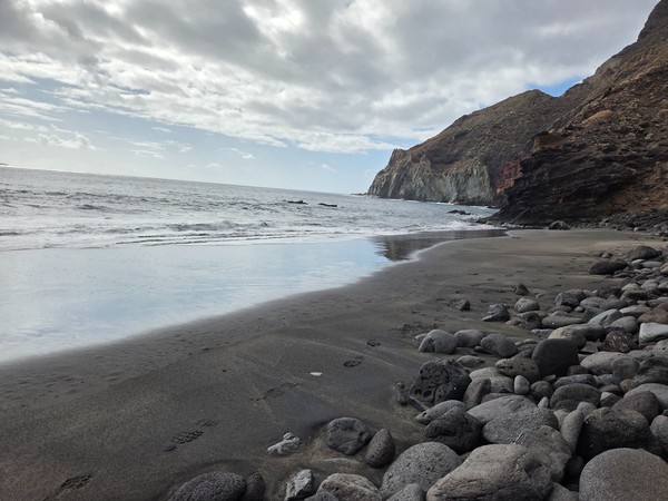 Low view from the sand at Playa Itamar Diez looking out to the Atlantic, with black sand in the foreground and cliffs closing the bay.
