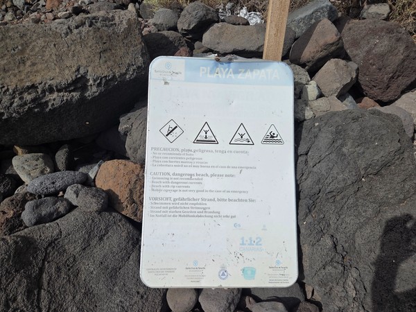 Warning sign on the rocks at Playa Itamar Diez, labelled Playa Zapata, advising that this is a dangerous beach with strong currents and limited mobile coverage.