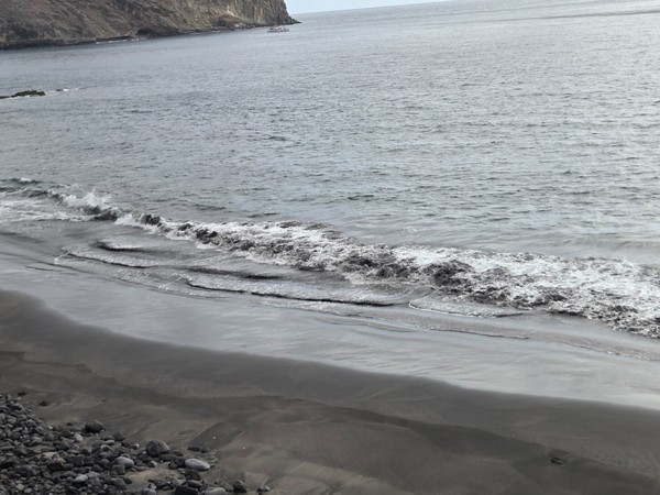 Central section of Playa Itamar Diez seen from above, with a broad expanse of black sand, scattered rocks and the calm ocean beyond.