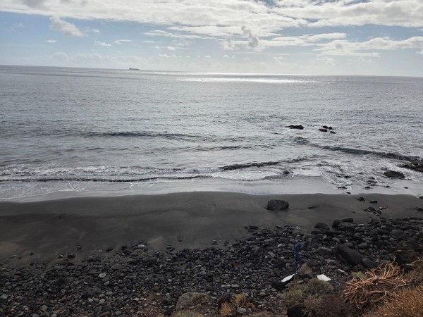 Close-up of small Atlantic waves gently rolling over the fine black sand of Playa Itamar Diez, highlighting the texture and subtle colour variations.