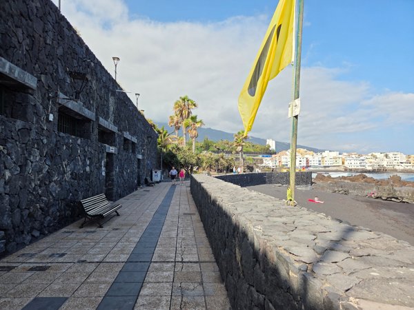 Volcanic-stone promenade and yellow flag overlooking the Charcón beach area.