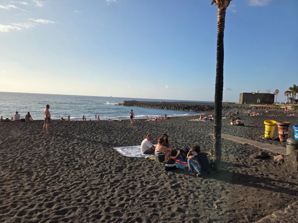 Late afternoon crowds relaxing on the black sand with the breakwater and San Felipe Castle in view.
