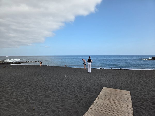 Visitors posing for photos on the dark volcanic sand near the shoreline.