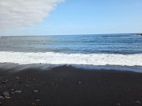 Small wave washing over the fine black sand of Playa Jardín.