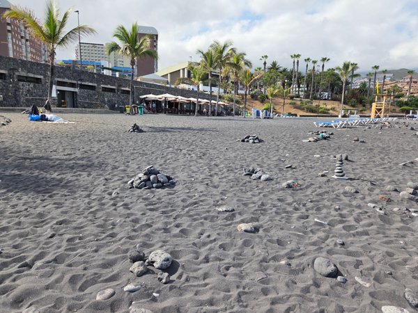 Small piles of rounded stones stacked on the wide sand area behind the sunbed zone.