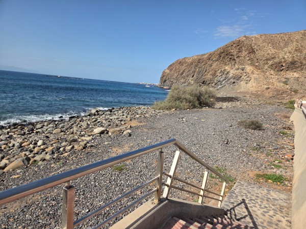 Staircase with metal handrail descending from the promenade to the stony shore beside the cliffs at Playa La Arenita.