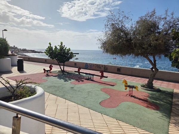 Small children’s play area with spring riders and trees next to the seaside promenade overlooking Playa La Arenita.