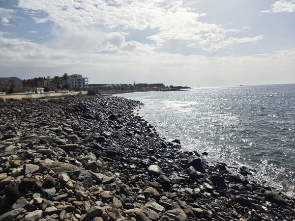 Wide rocky shoreline at Playa La Arenita covered with different sizes of volcanic stones leading into the Atlantic Ocean.
