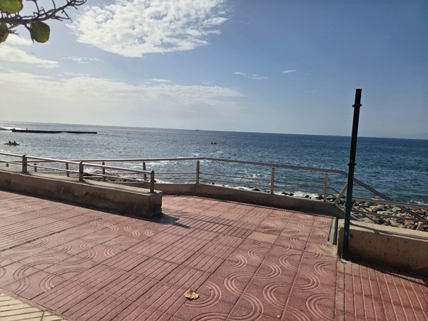 Seafront promenade at Playa La Arenita with a paved path, railing and rocky beach below on a bright day.