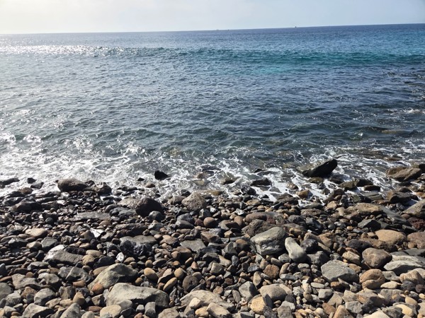 Clear Atlantic waves breaking gently over rounded volcanic stones on the shoreline of Playa La Arenita.