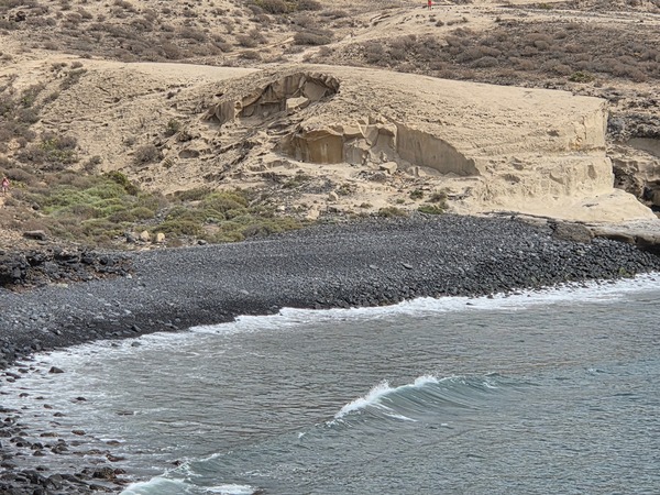 Close view of the pale sandstone tuff above the dark pebble beach at Playa Pardela.
