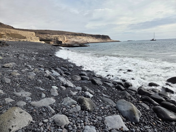 Low-angle view across the pebble slope with waves washing the stones on Playa Pardela.