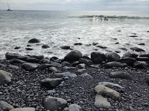 Foamy shore break rolling over rounded volcanic boulders on the edge of the cove.