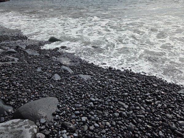 Close-up of smooth black pebbles and larger stones glistening with sea spray.