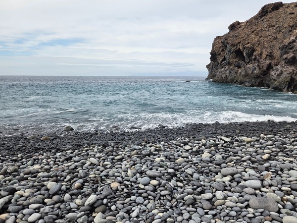 Close view of rounded black volcanic pebbles and stones covering the beach at Playa de Ricasa.