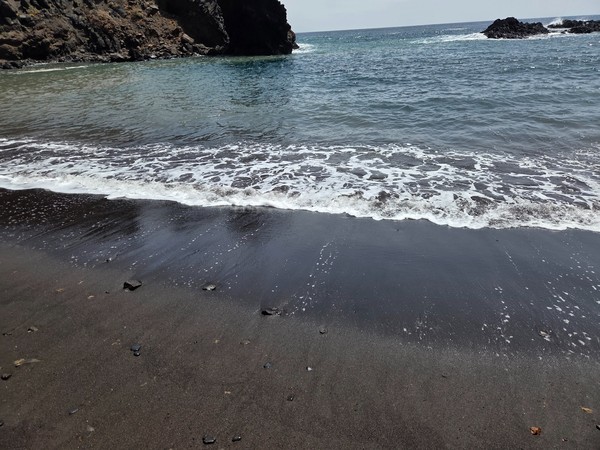 Small Atlantic waves washing the fine black sand on Playa de Roque Bermejo during calm sea conditions.