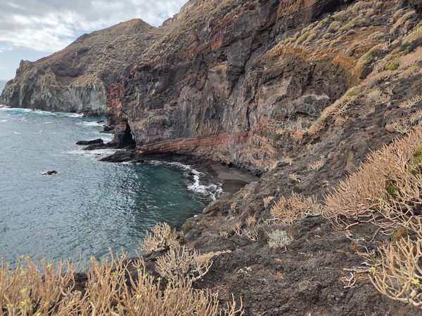 Wide panoramic view of the rugged volcanic coastline near Playa de Zapata in Tenerife, with steep cliffs, dark rocks and the Atlantic Ocean under a cloudy sky.