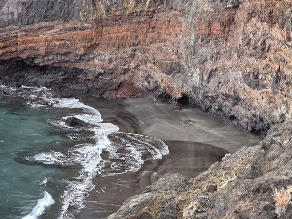 Another angle of Playa de Zapata showing the black sand cove, the turquoise water and the towering multicoloured volcanic cliffs above the shoreline.