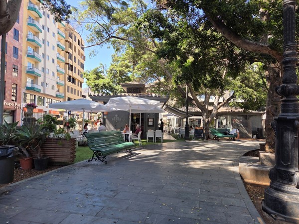Outdoor café kiosk with umbrellas and green benches at Plaza del Príncipe de Asturias.