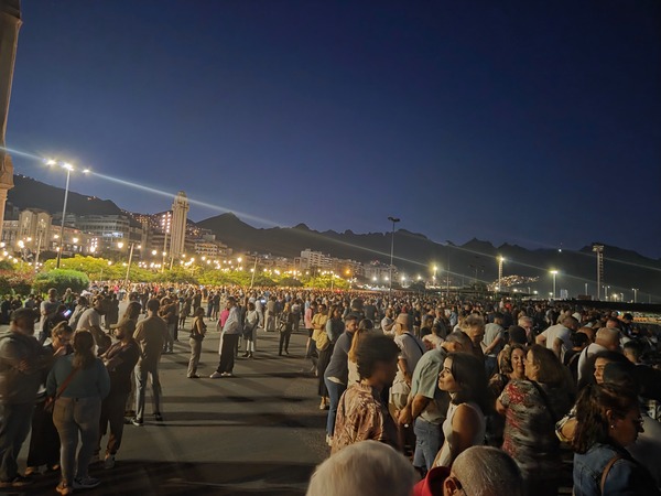 Wide view of Avenida de Anaga with a large crowd and the Anaga mountain skyline as night falls during Plenilunio in Santa Cruz.