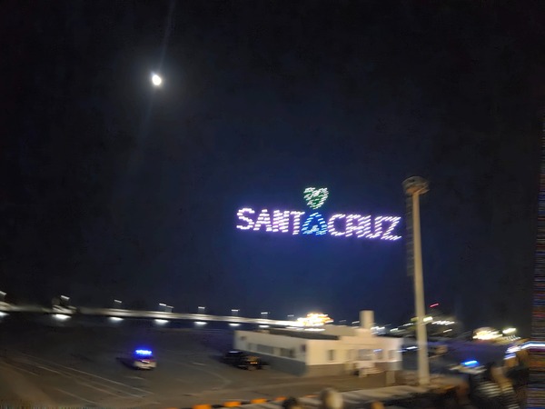 Drones spelling the words SANTA CRUZ with a small green heart above, floating over the port during Plenilunio.