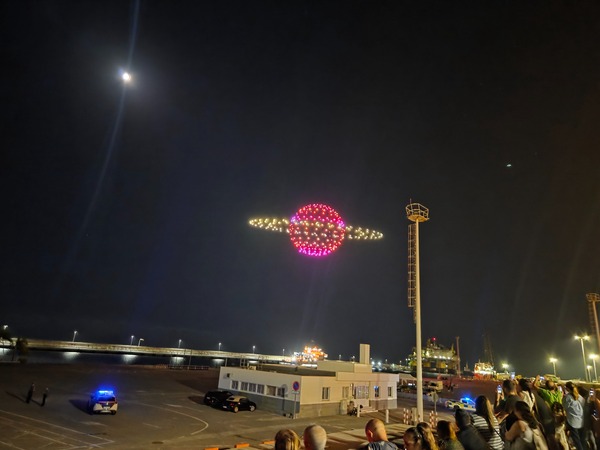 Ringed planet shape—like Saturn—created by red and yellow drones in the sky during Plenilunio at the port.