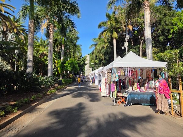 Row of stands with colorful summer clothing and accessories along the palm avenue. Taken at Plenilunio 2025 in García Sanabria Park, Santa Cruz de Tenerife.