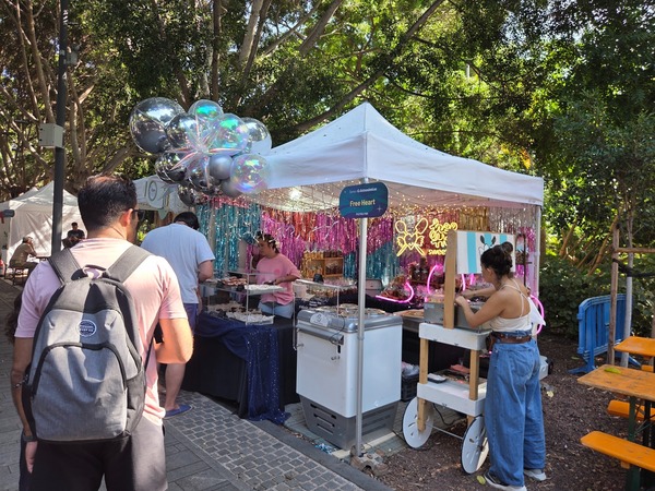 Free Heart sweets booth sparkling with balloons, neon and trays of churros and treats. Taken at Plenilunio 2025 in García Sanabria Park, Santa Cruz de Tenerife.