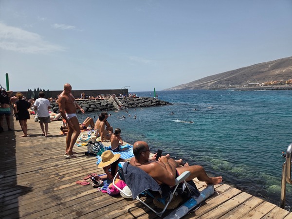 Wooden platform with swimmers enjoying calm waters at the muelle of El Puertito de Güímar.