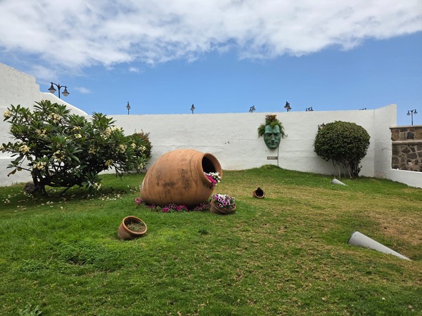 Garden installation with large terracotta amphora and a green face sculpture on a lawn in Puerto de la Cruz.