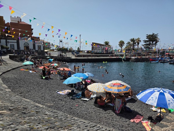 Harbour cove at Puerto de la Cruz with families on the pebble shore and colourful bunting over the water.