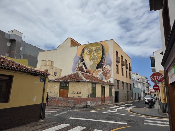 Large mural of an elderly artisan on a corner building in the historic streets of Puerto de la Cruz.
