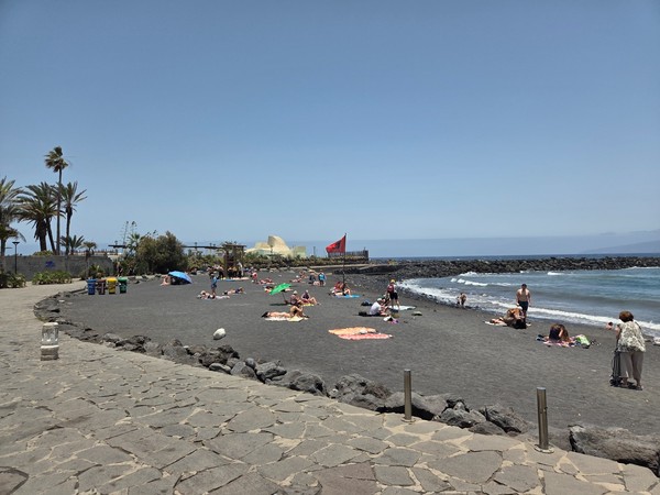Black-sand beach near Lago Martiánez with sunbathers and gentle Atlantic waves.